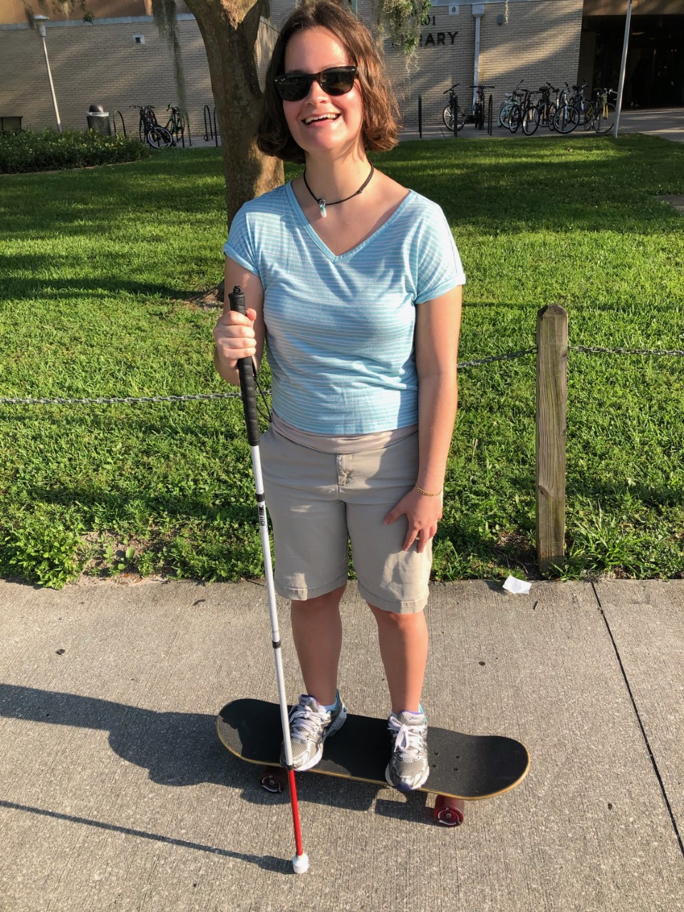 Claudia, a USF student, rides a skateboard with her white cane