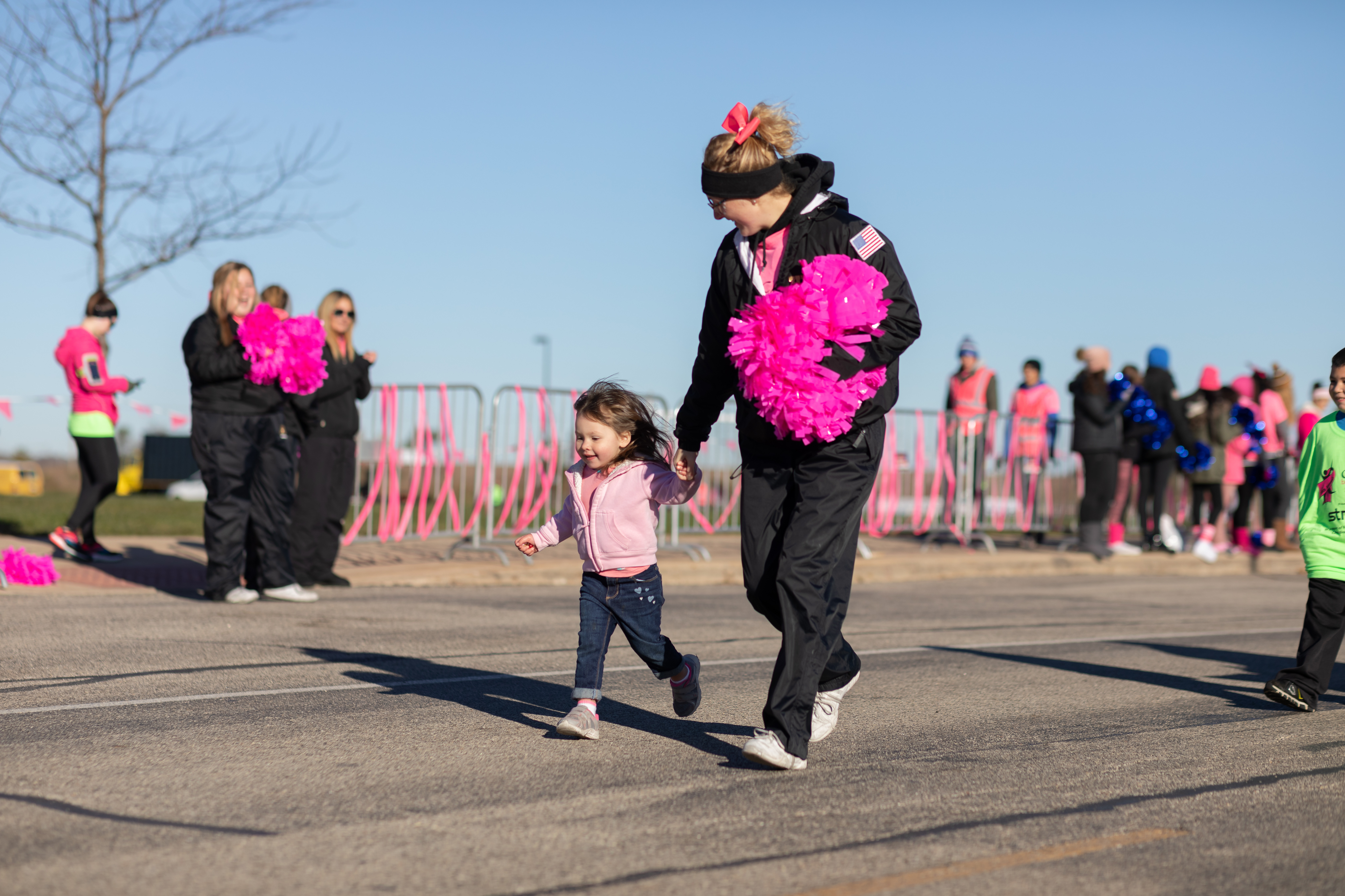 A cheerleader helping a little girl cross the finish line.