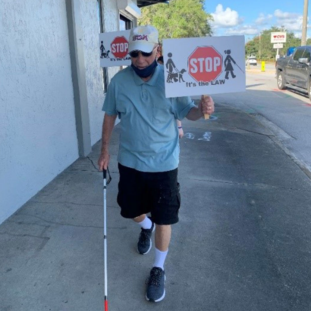 Supporters walk with white canes and signs on White Cane Awareness Day.