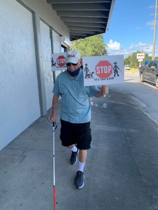 Joe Mastrodomenico walks with his cane and awareness sign