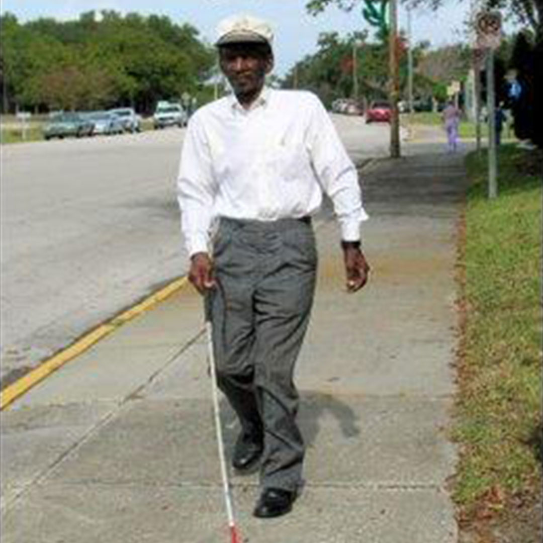An older gentleman navigates the sidewalk with his white cane.