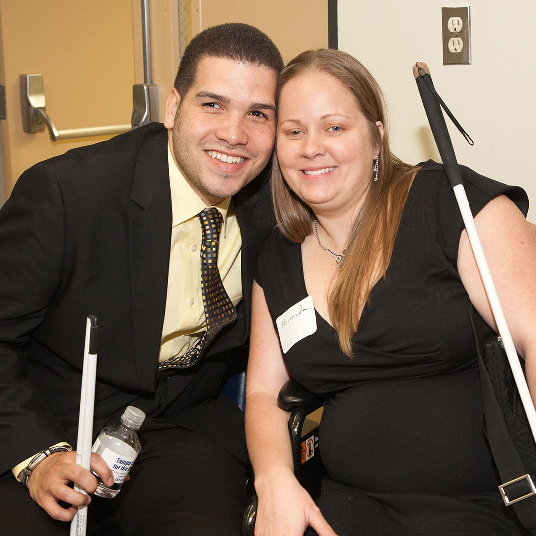 A man and woman holding white canes enjoy a business event.